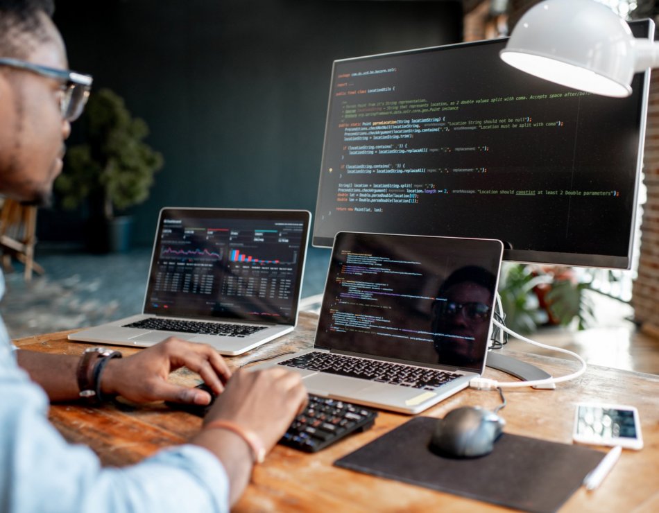 Business person typing code on three monitors.